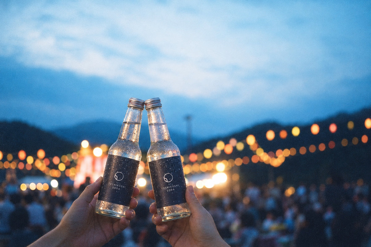夏祭りの提灯の下で年越しソーダを掲げる二人の手元
