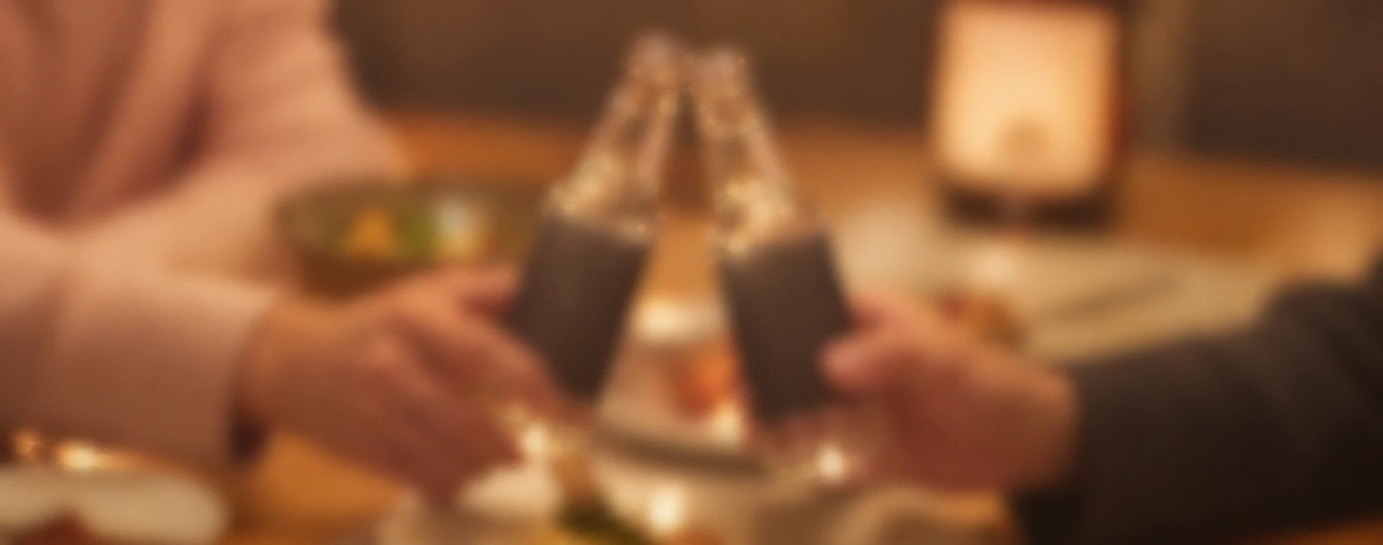 食卓で瓶を合わせて乾杯する二人